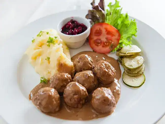 Meatballs in cream sauce with mashed potato, red berries, tomato and sliced cucumber