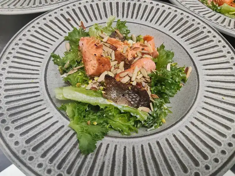 Seared salmon on salad leaves with almond flakes, on a ribbed grey plate