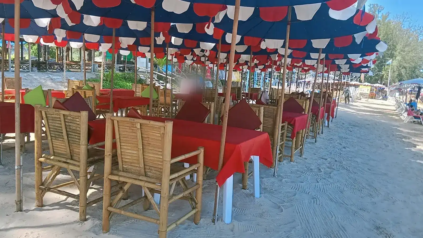 Bamboo chairs and red tables on the sand under navy umbrellas with red and white flaps