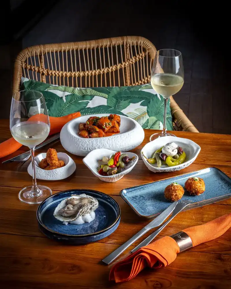 A table set with small plates, an oyster, croquettes and two glasses of white wine