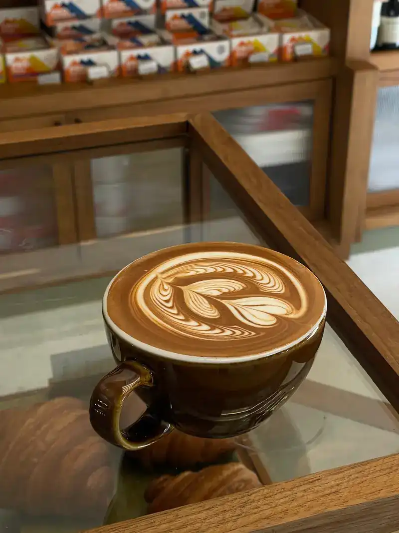 A latte with leaf art on the glass top of a display counter, pastries underneath