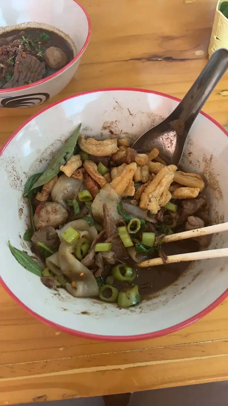 Wide rice noodles in dark broth with crispy pork and spring onion