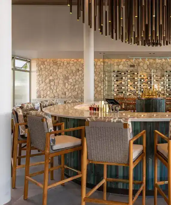 Round indoor bar with woven stools, a stone wall and a hanging brass light