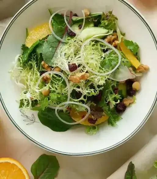 Salad of frisée, citrus, walnuts and cranberries in a white bowl with a green rim
