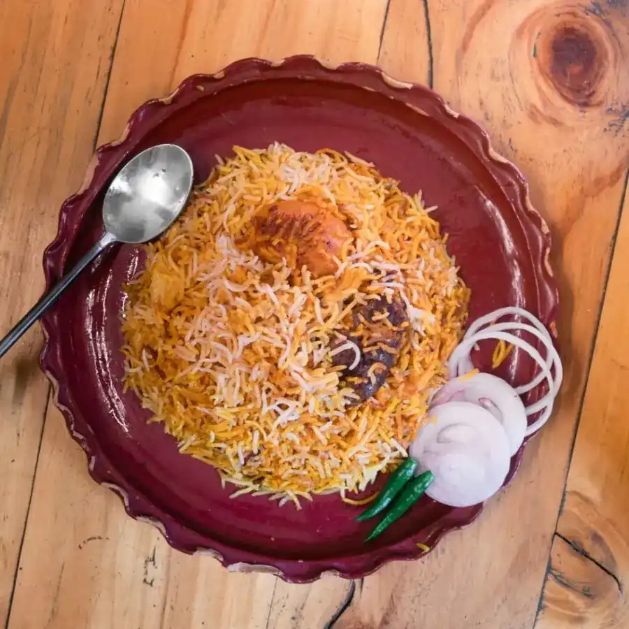 Biryani on a dark red scalloped plate with onion rings and green chillies, seen from above