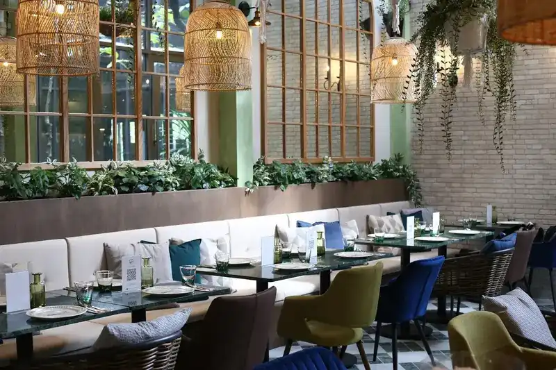 A long banquette under a planter of green leaves, with rattan lamps and hanging plants above