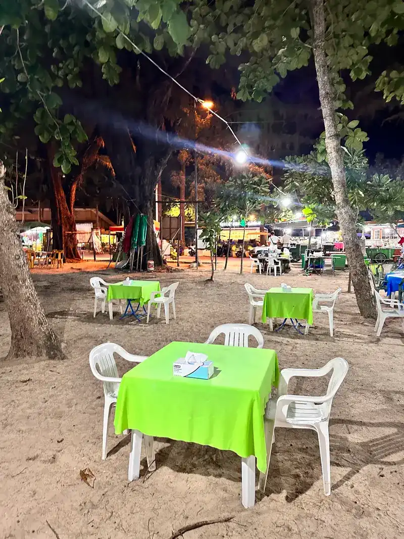 Tables with lime-green cloths on the sand at night, lit by lamps in the trees