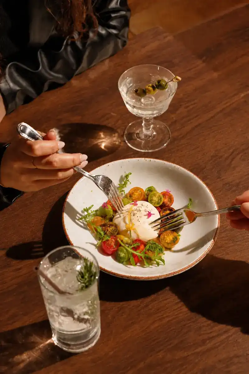Two forks reaching into a bowl of burrata with heirloom tomatoes