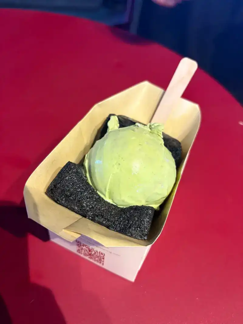 Matcha ice cream on a black grilled bun in a paper tray on a red table