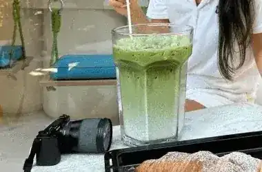 An iced matcha in a tall glass on the window counter at Matchoya, a croissant tray in front and the rope swing seat behind