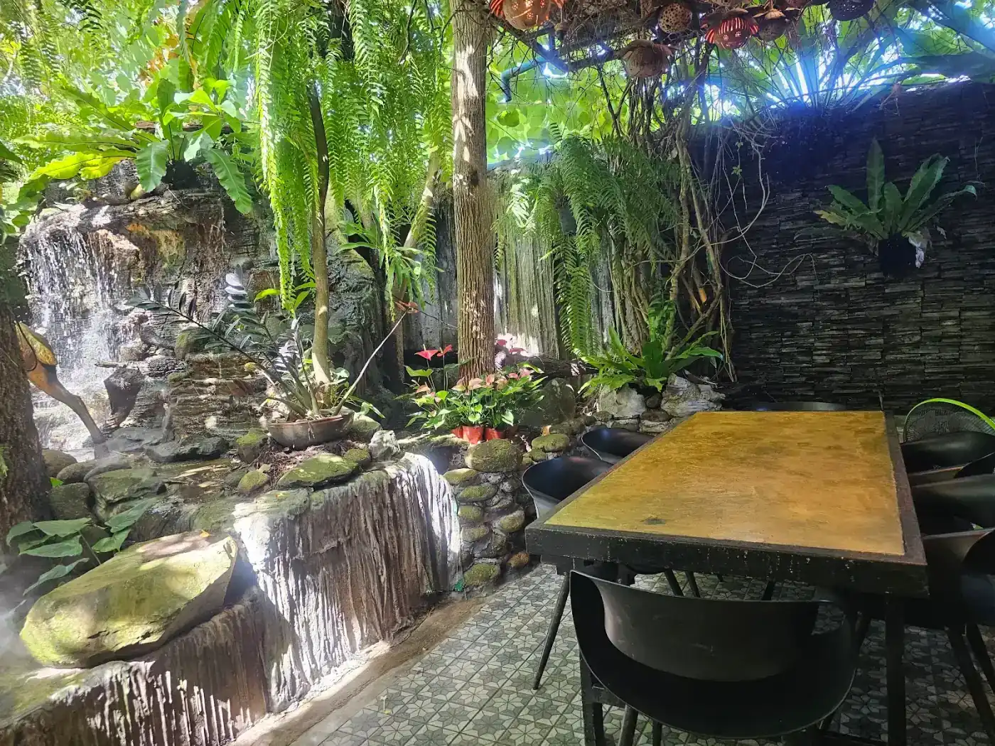A table beside the garden waterfall at Ta Tuay, under ferns and hanging lamps