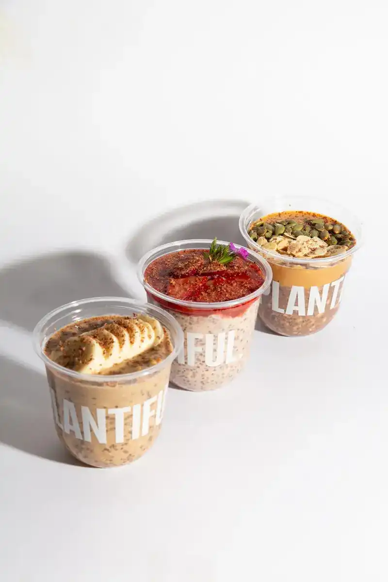 Three takeaway cups topped with banana, strawberry and pumpkin seeds