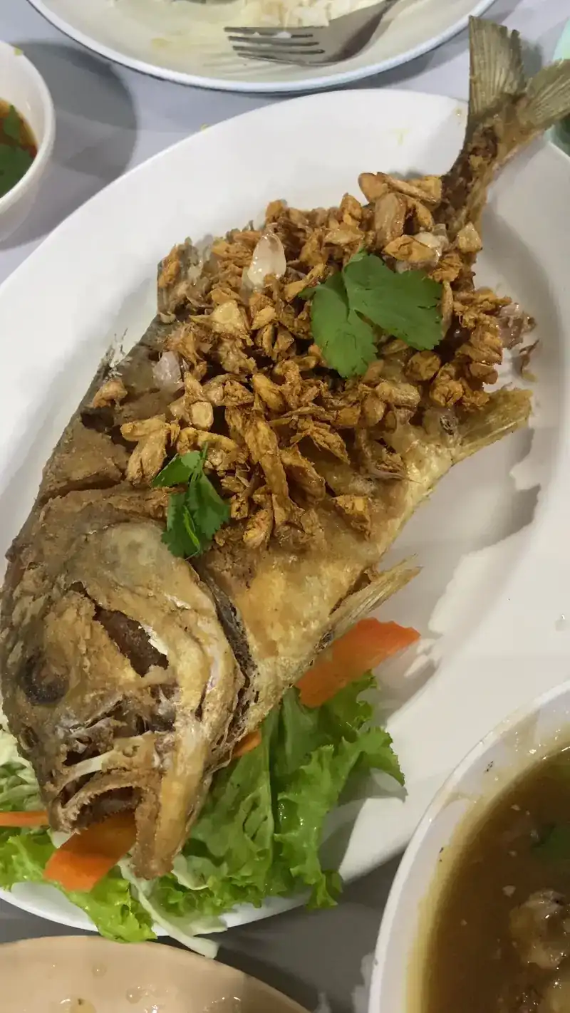 A whole fried fish on lettuce, with a crisp golden topping and coriander