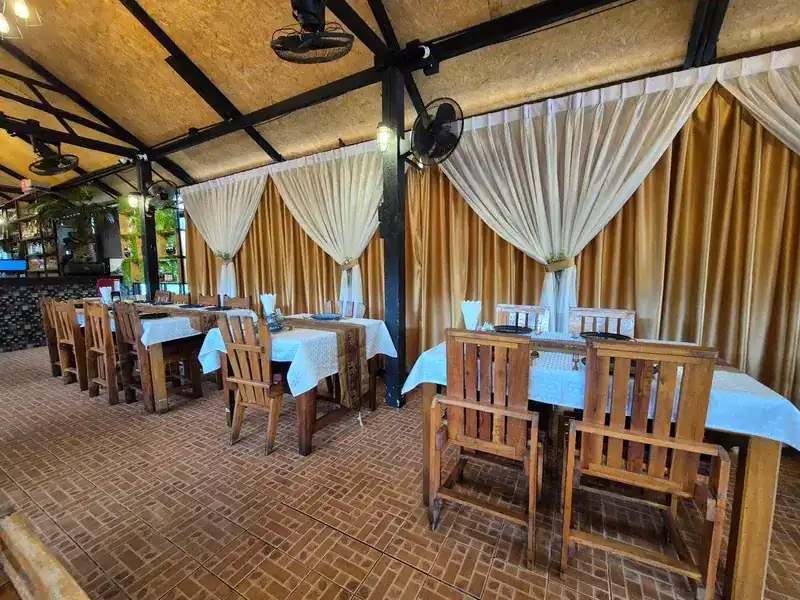 Dining room with wooden chairs, white tablecloths and cream curtains tied back over gold drapes