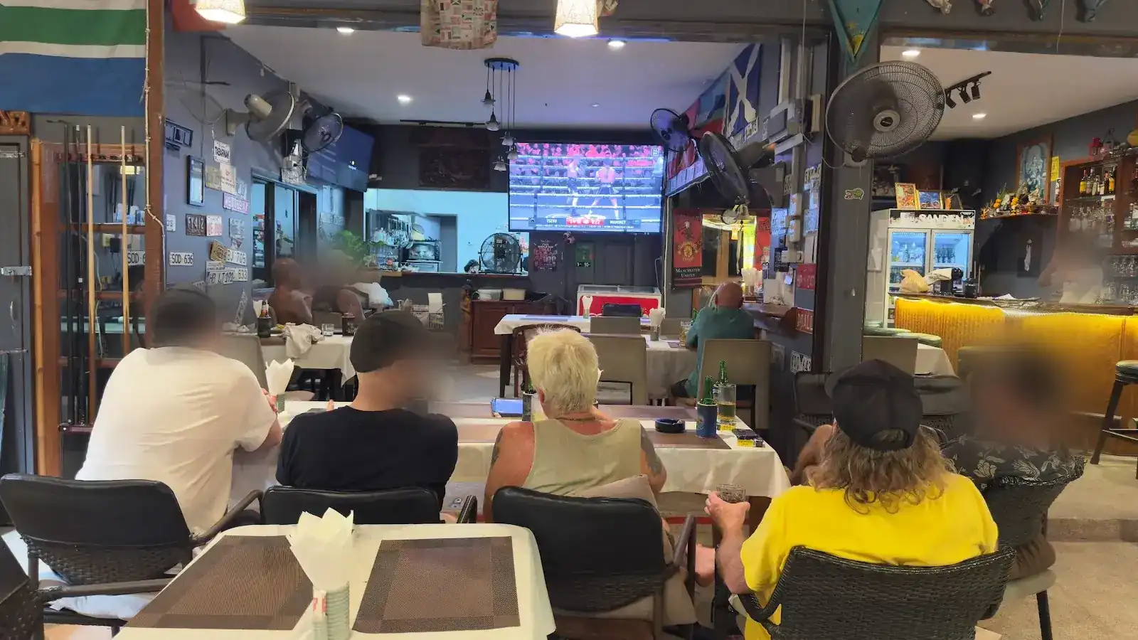 Guests watching boxing on the big screen at Nok & Jo’s, with flags and old number plates on the walls