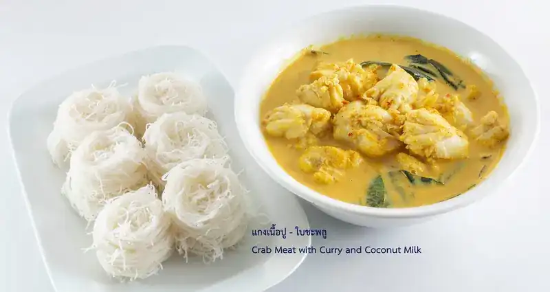 A bowl of yellow crab curry with large pieces of crab meat and betel leaves
