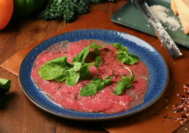 Beef carpaccio with rocket on a blue plate