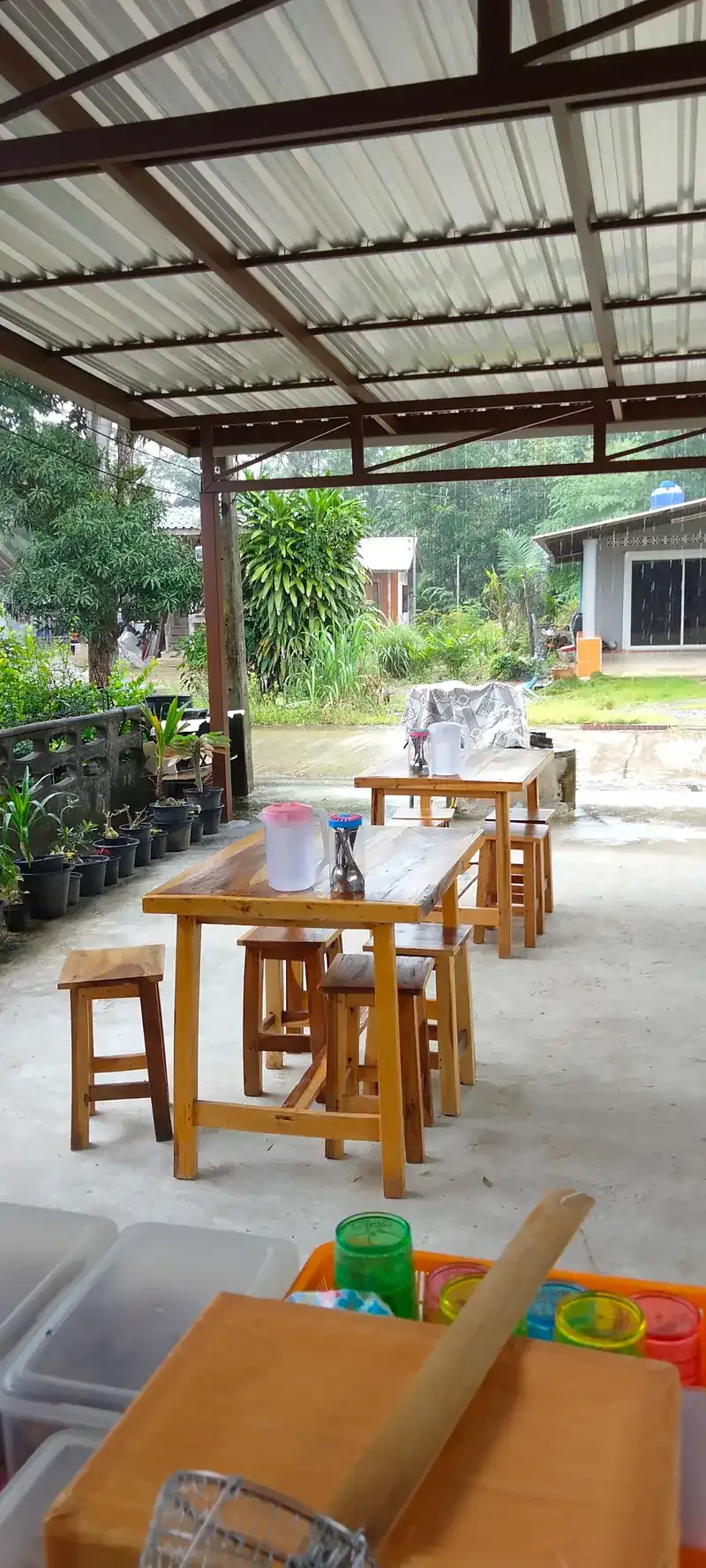 Rain beyond the roof, wooden tables and stools, and a pestle resting on the counter