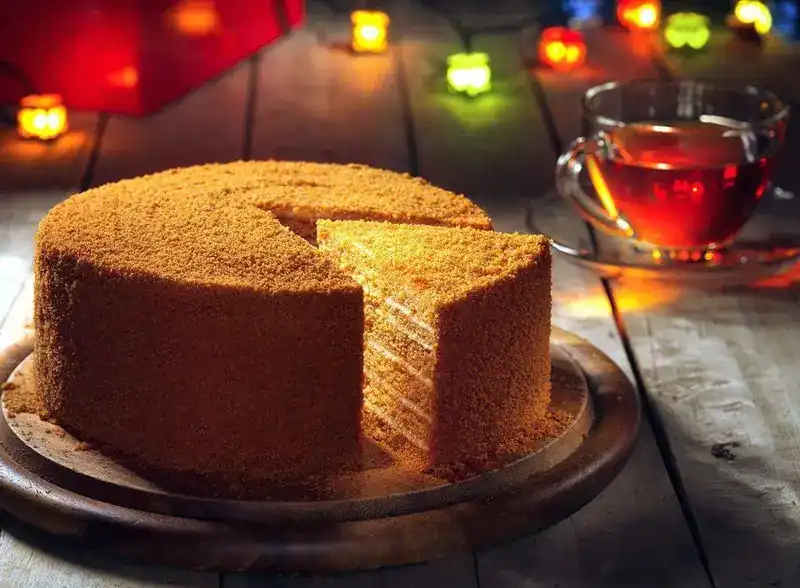 A layered honey-coloured cake with one slice cut, and a glass cup of tea