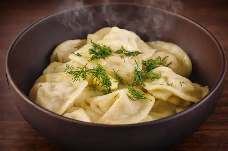 A dark bowl of steaming dumplings scattered with fresh dill