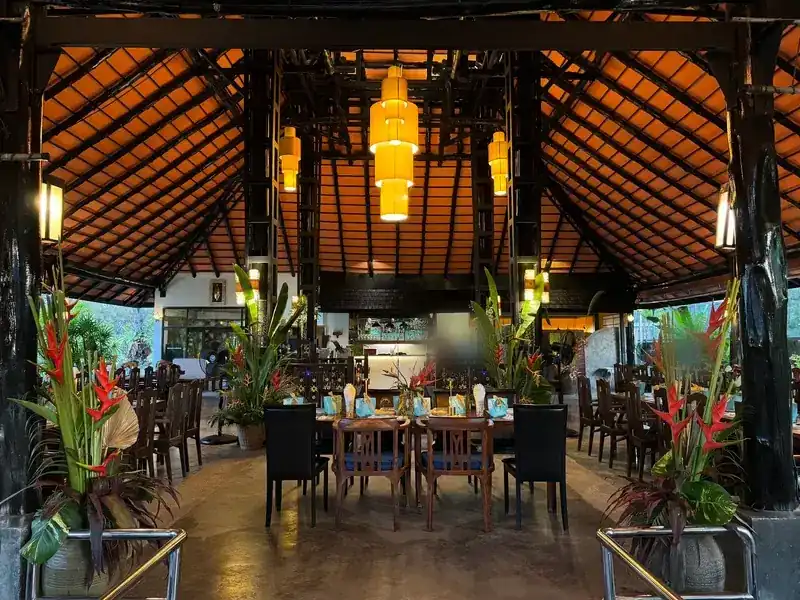 Inside the main pavilion: a high orange-tiled roof, tall amber lanterns and red heliconia beside a laid table