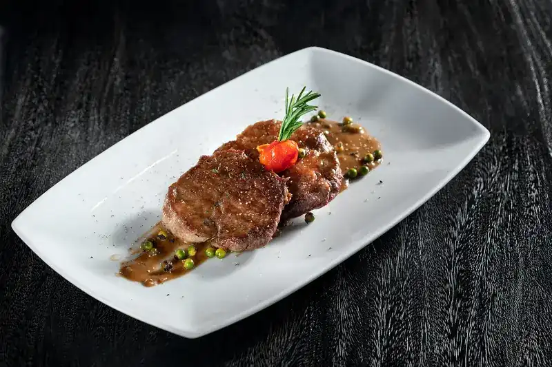 Beef medallions with pepper sauce and green peppercorns on a white plate