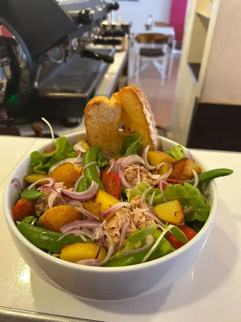A salad bowl with roast potatoes, green beans, red onion and toasted bread, the espresso machine behind