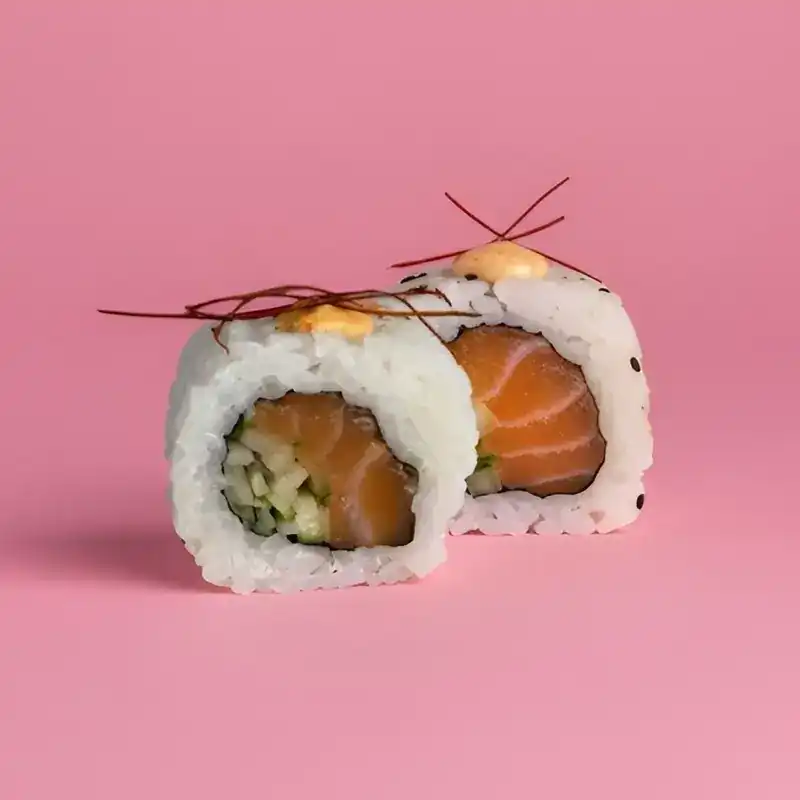 Two pieces of spicy salmon roll with chilli threads on a pink background