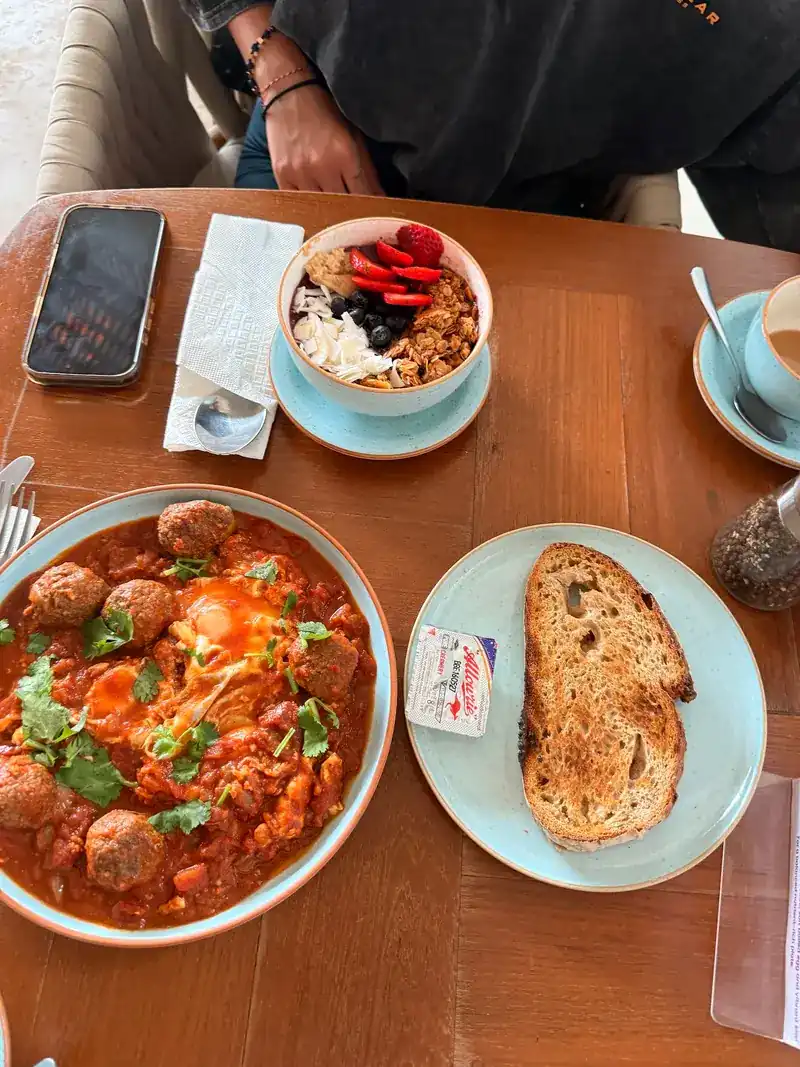 Eggs in tomato sauce with meatballs, sourdough toast and a bowl of granola with berries