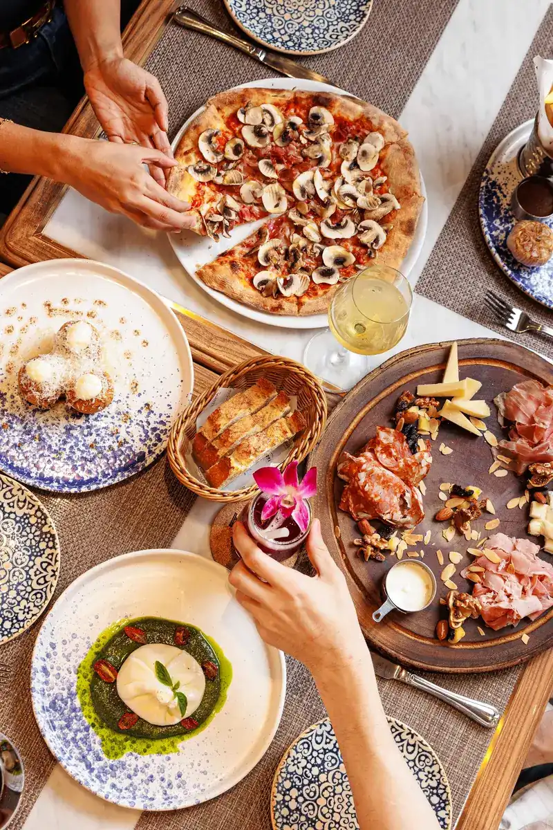 A shared table from above: mushroom pizza, a board of cured meats, burrata on pesto and a basket of bread