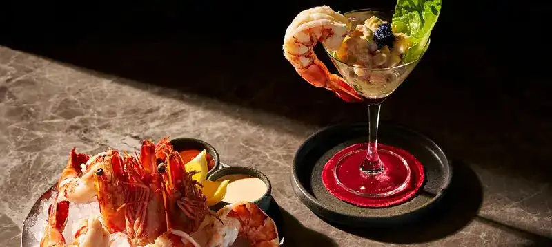 Tiger prawns on ice beside a prawn cocktail in a coupe glass