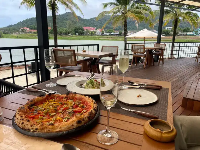A pizza on a table on the deck, the lake behind