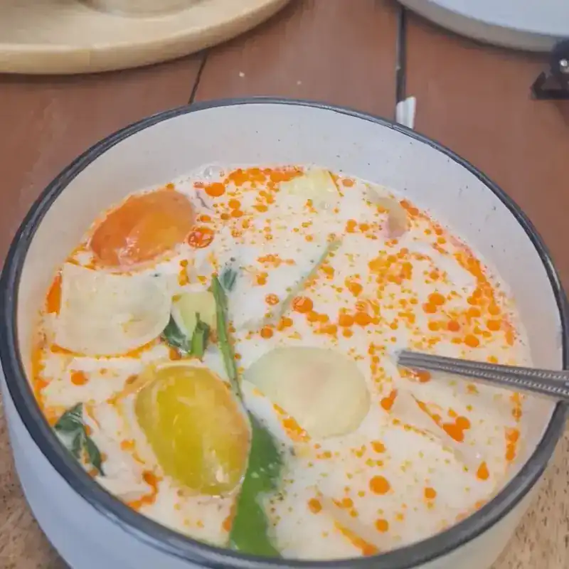 A bowl of creamy Thai soup with chilli oil, tomato and mushrooms