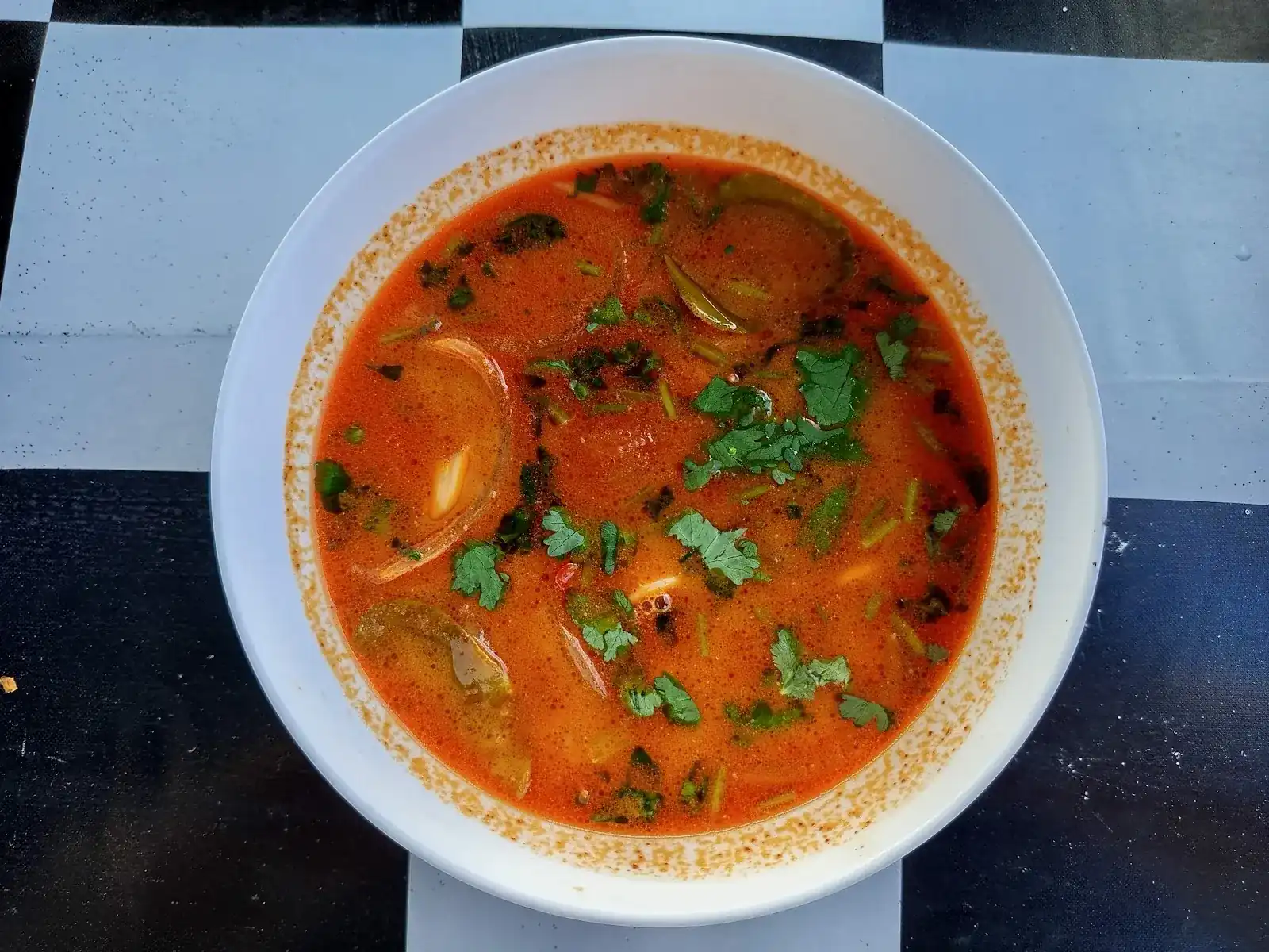 Tom yum in a white bowl on a black-and-white chequered table