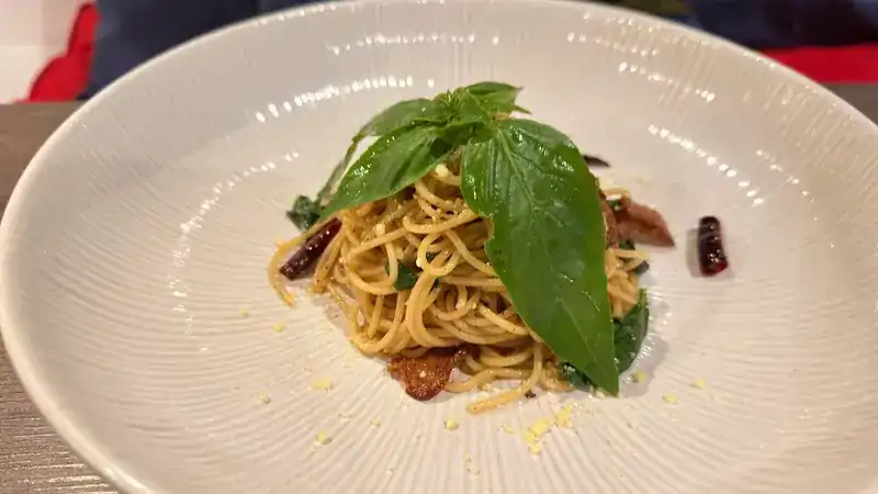 Spaghetti with basil leaves and dried chilli in a wide white bowl