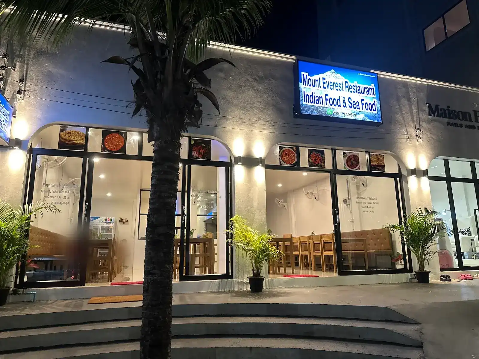 Mount Everest Restaurant at night: the lit blue sign over two glass shopfronts with wooden tables inside
