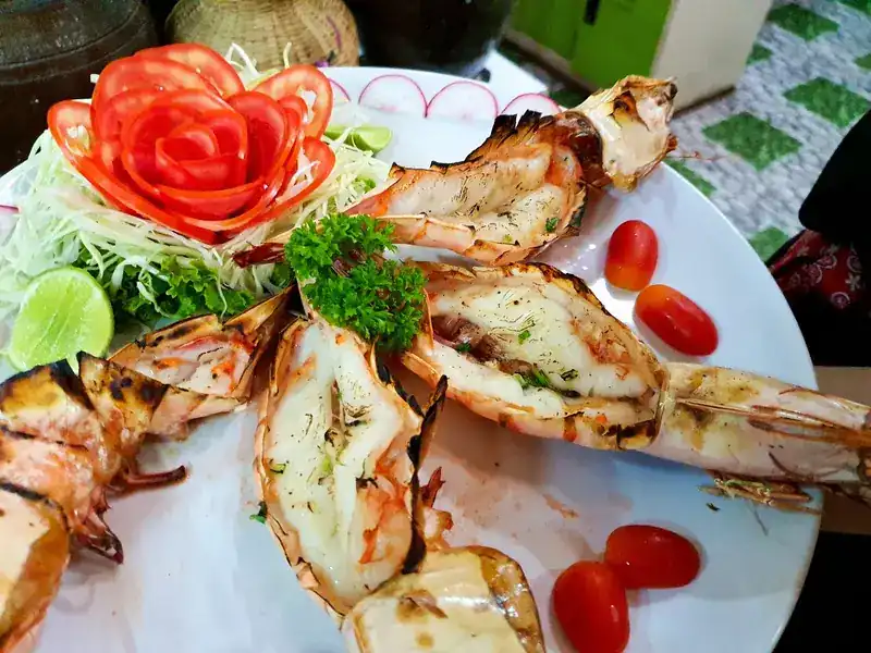 Grilled prawns split open, with a tomato carved into a rose, lime and shredded cabbage