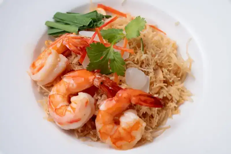 Crispy sweet noodles topped with prawns on a white plate