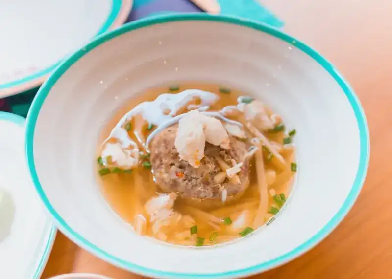 A clear soup with crab in a white bowl with a turquoise rim