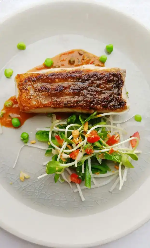 Pan seared fish fillet with a salad of pea shoots, sprouts and tomato on a pale plate