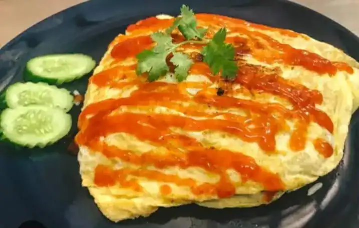 An omelette with chilli sauce, coriander and sliced cucumber