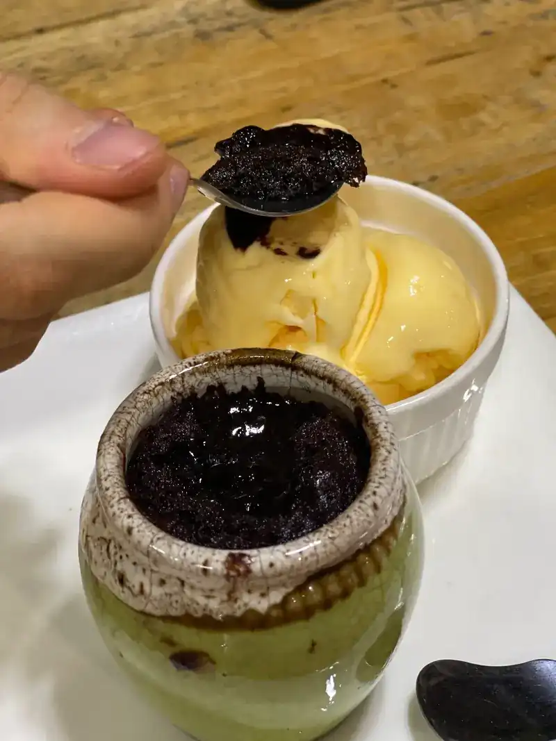 A dark pudding in a small stoneware pot, with a scoop of ice cream