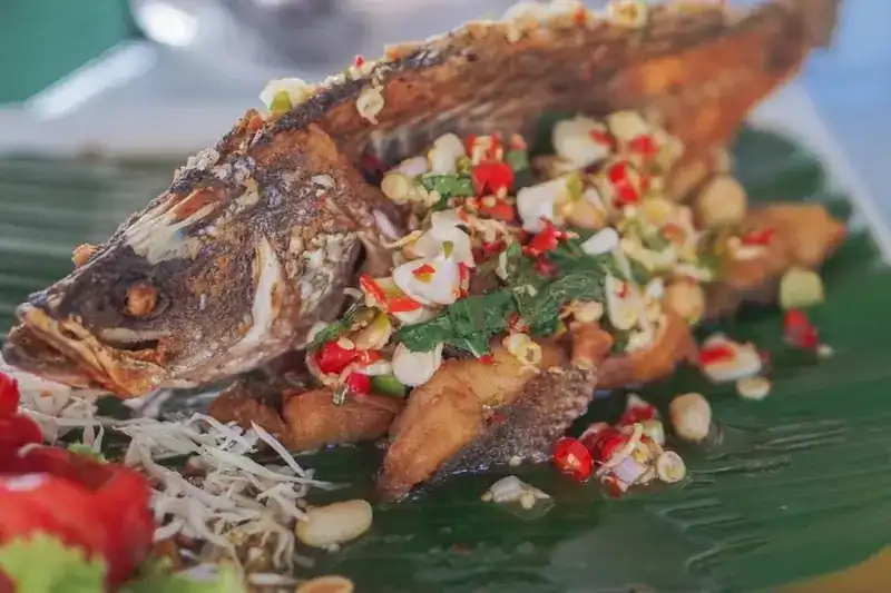 A whole fried fish on banana leaf, topped with chilli, herbs and nuts