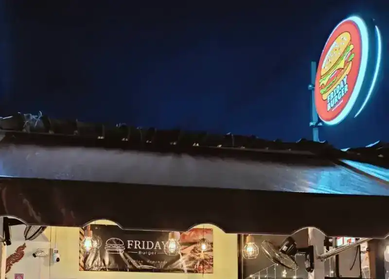 The Friday Burger shopfront at night: the round lit sign above the roof and the name banner over the door