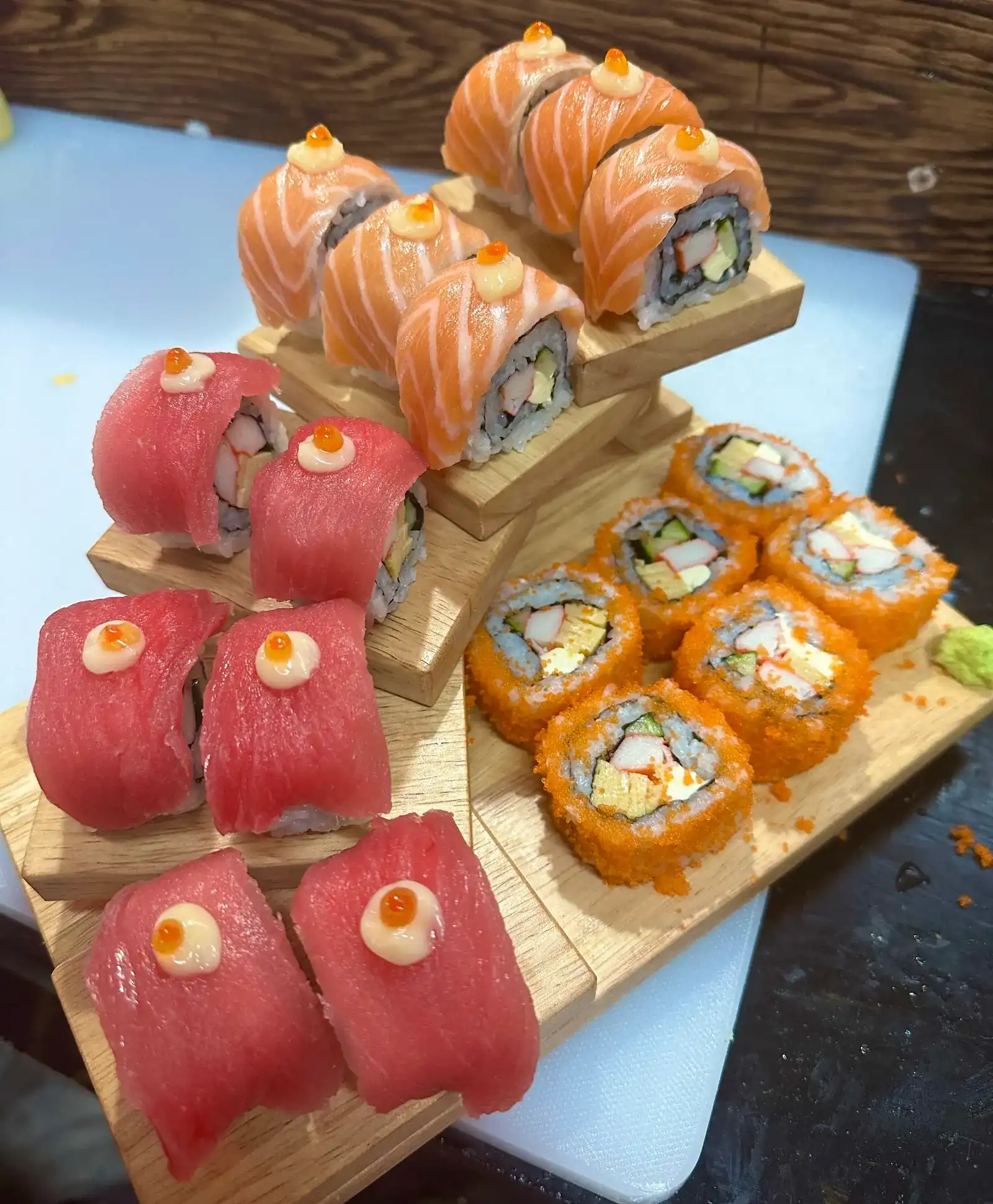 Tuna and salmon rolls topped with roe on stepped wooden stands, beside a row of tobiko rolls