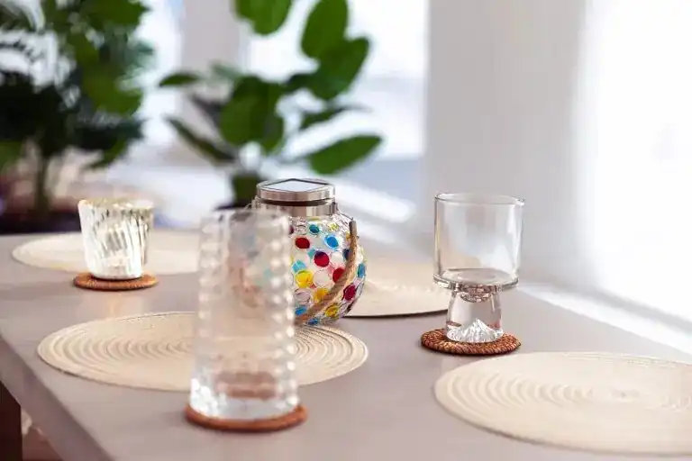Cut-glass tumblers and a beaded glass lantern on woven placemats in bright daylight