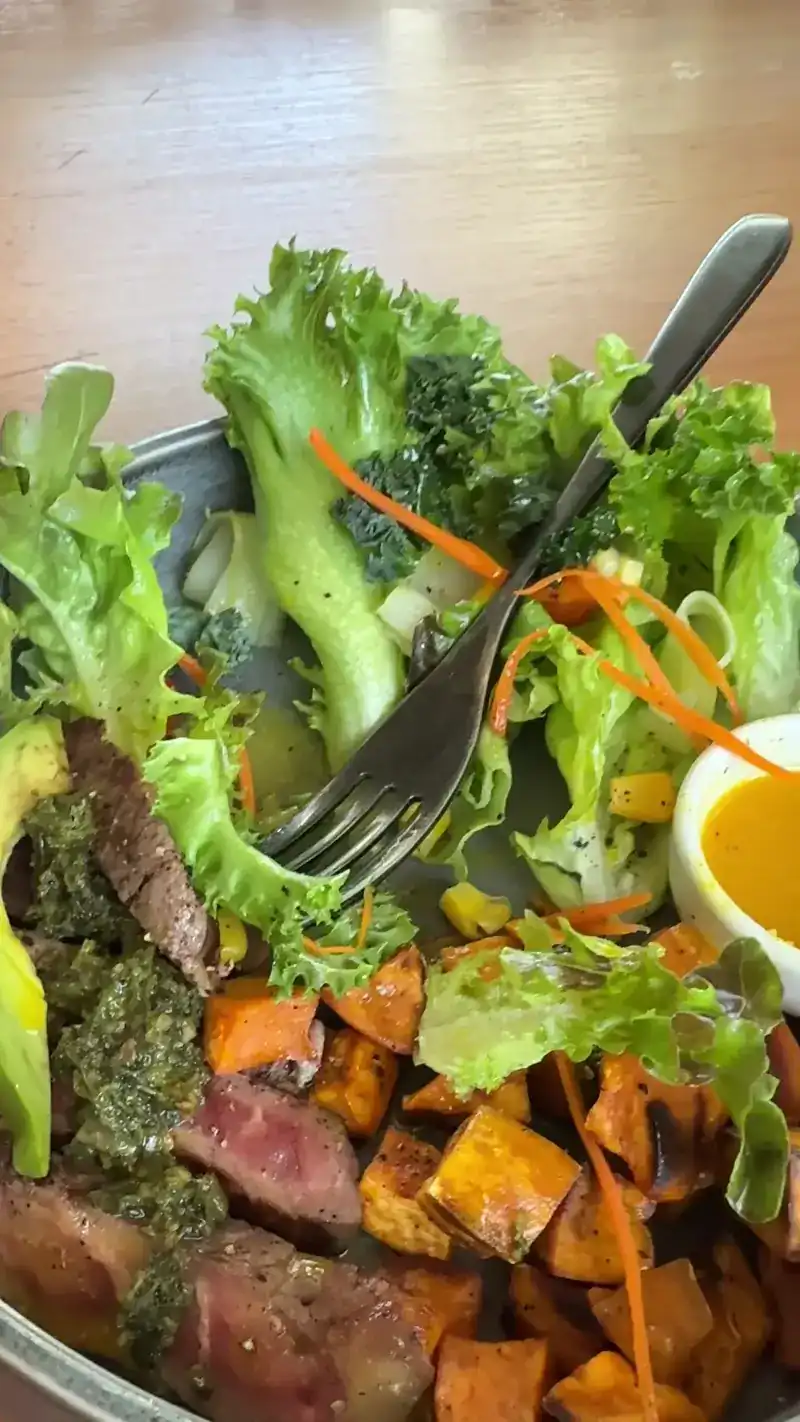 A salad of greens and roasted sweet potato with sliced steak, green sauce and a soft egg