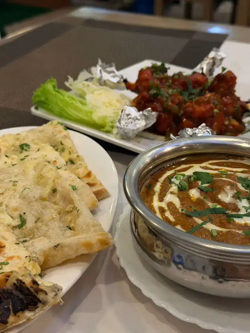 Herb-topped naan beside a creamy curry, with a spicy starter behind