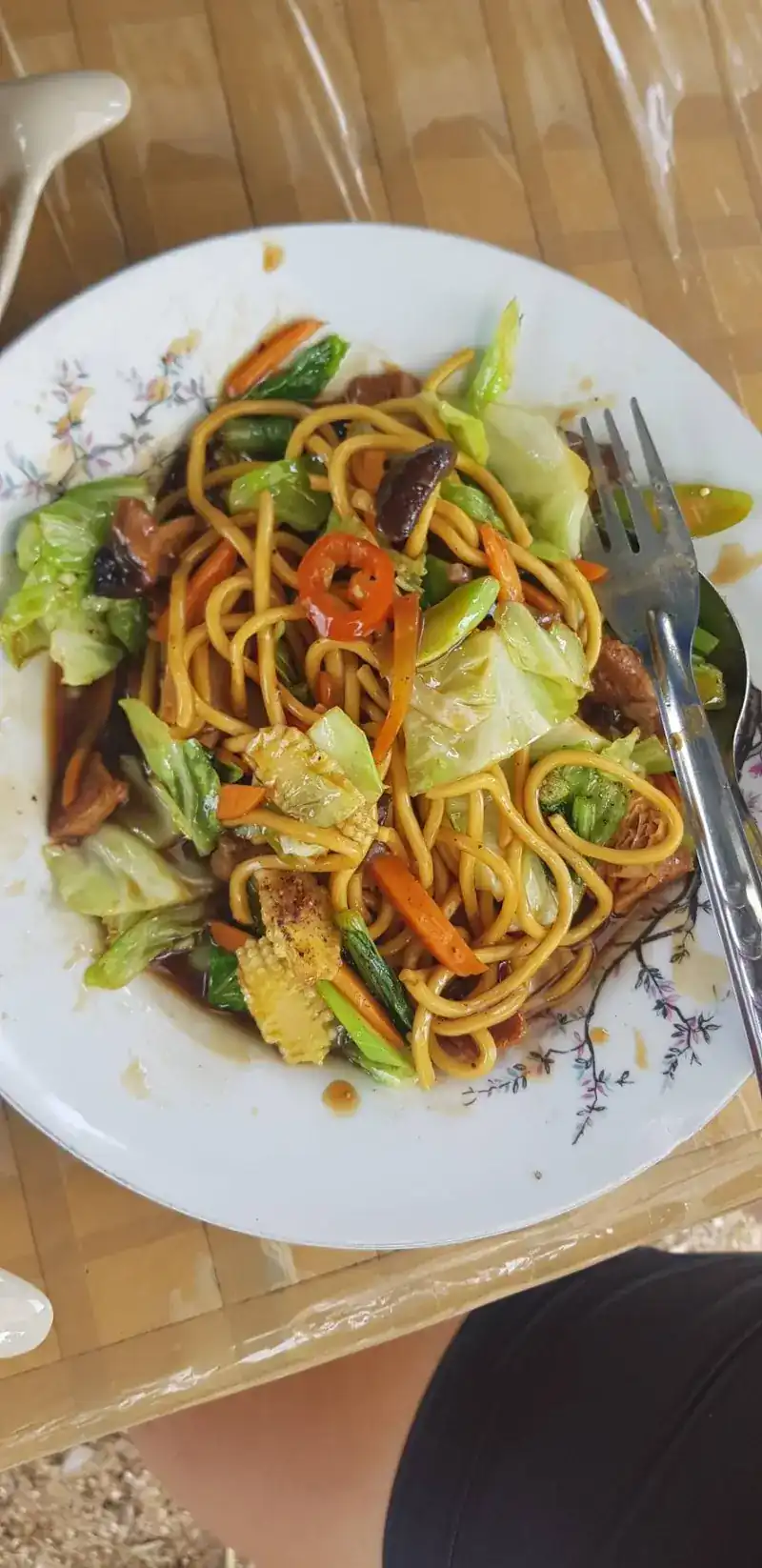 Yellow noodles stir-fried with cabbage, carrot, baby corn, mushrooms and chilli on a flowered plate
