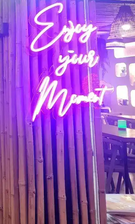 Pink neon sign reading Enjoy your Moment on a bamboo wall / ป้ายไฟนีออนสีชมพูเขียนว่า Enjoy your Moment บนผนังไม้ไผ่